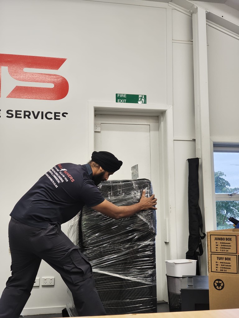 Office relocation Auckland — Big Bull Movers professional packing a large office item in protective blankets and wrap