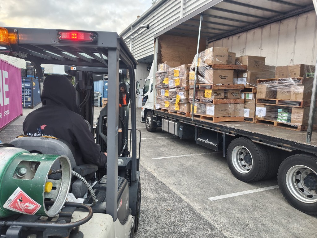 Industrial machinery movers Auckland — Big Bull Movers team loading palletized warehouse stock into a removal truck with a forklift