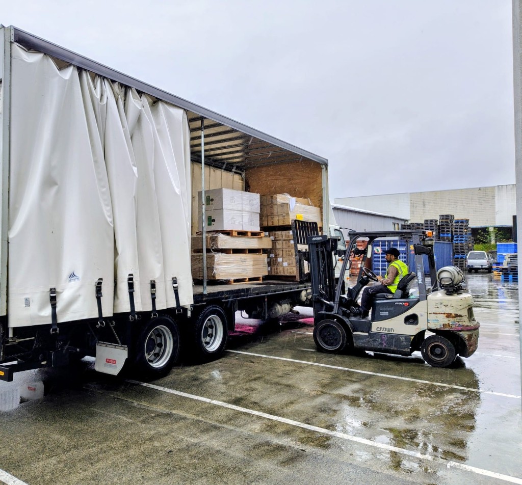 Commercial warehouse movers Auckland — Big Bull Movers forklift loading palletized cargo into a curtain-side truck at an industrial loading bay